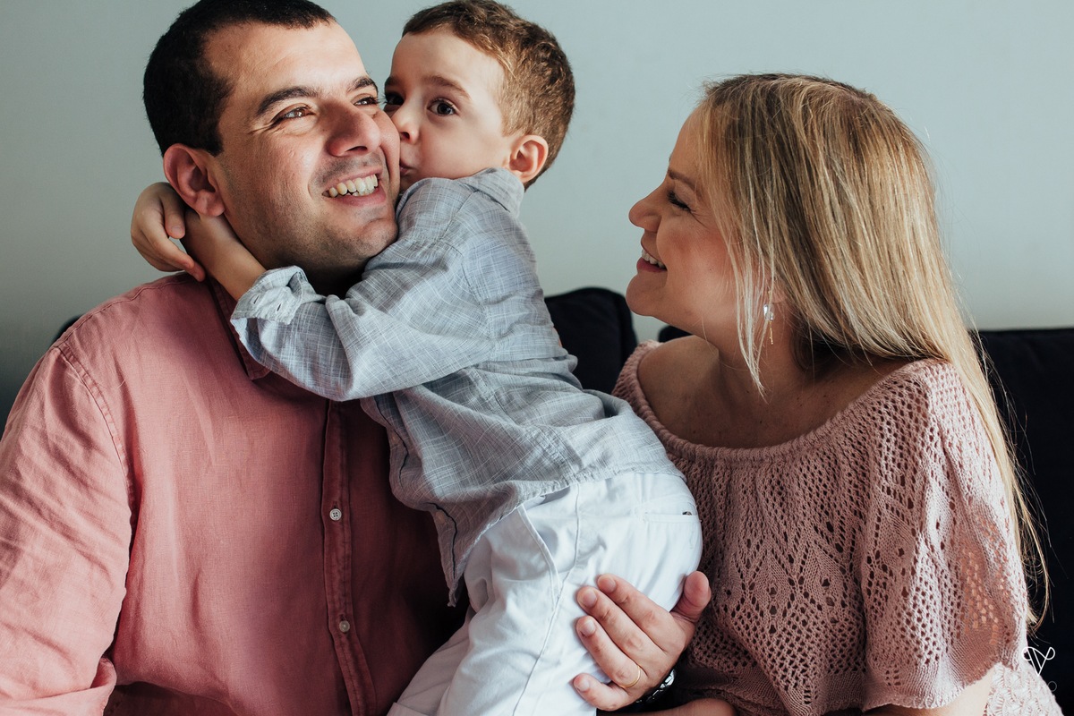 pai, mãe e filho se divertem em sessão fotográfica no sofá da sala