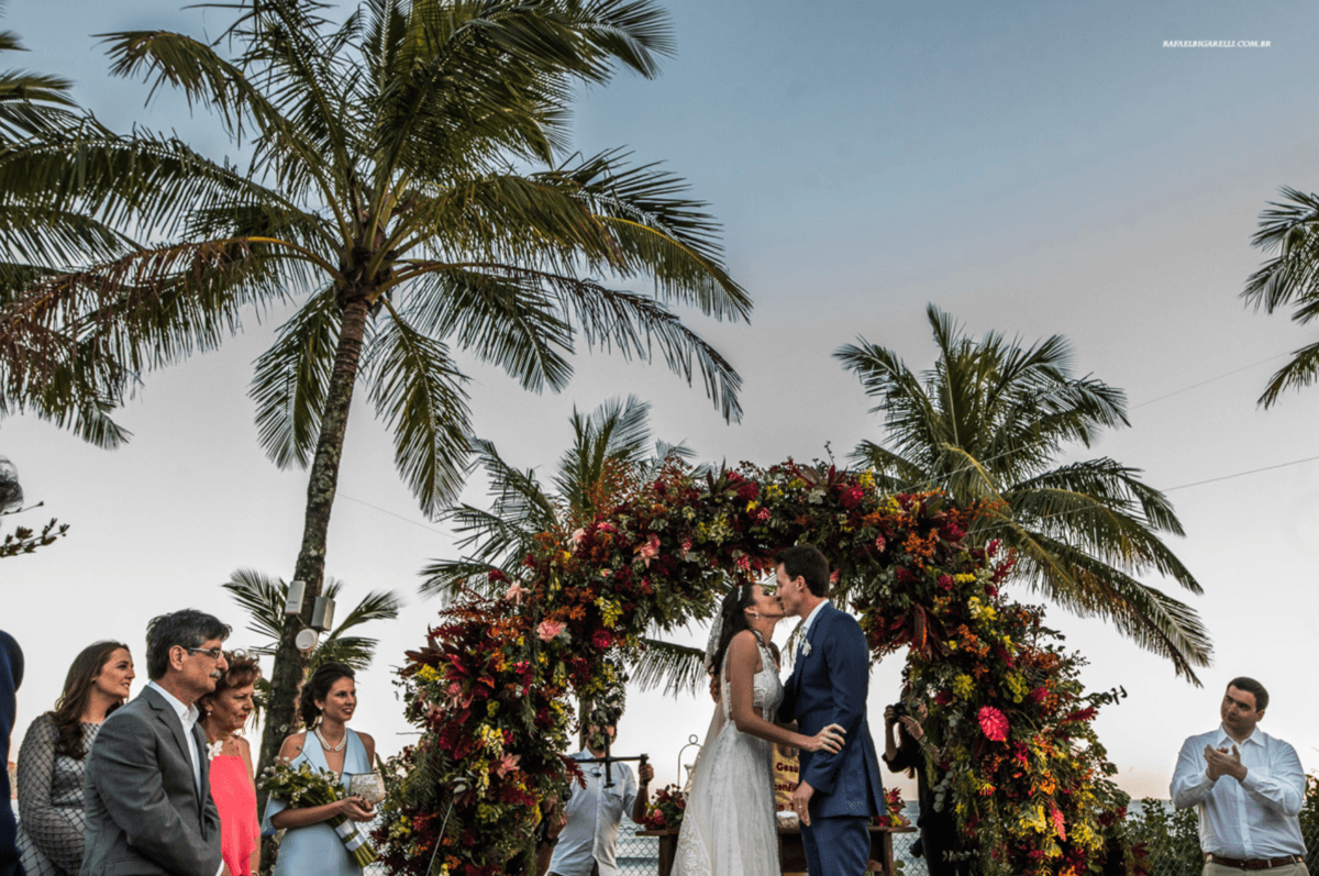 casal se beijando na frente de arcos de flores em decoração em casamento na praia em maresias sp fotógrafo rafael bigarelli