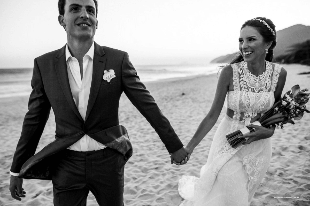 noivos de mãos dadas noiva com vestido de renda segurando o buquê em casamento na praia de maresias litoral norte de são paulo fotografia rafael bigarelli
