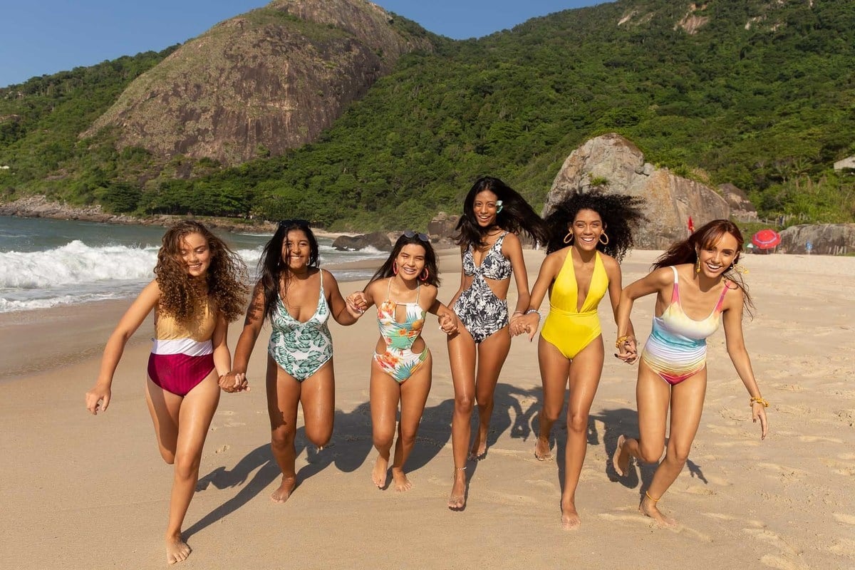 meninas de mãos dadas correndo na areia da praia