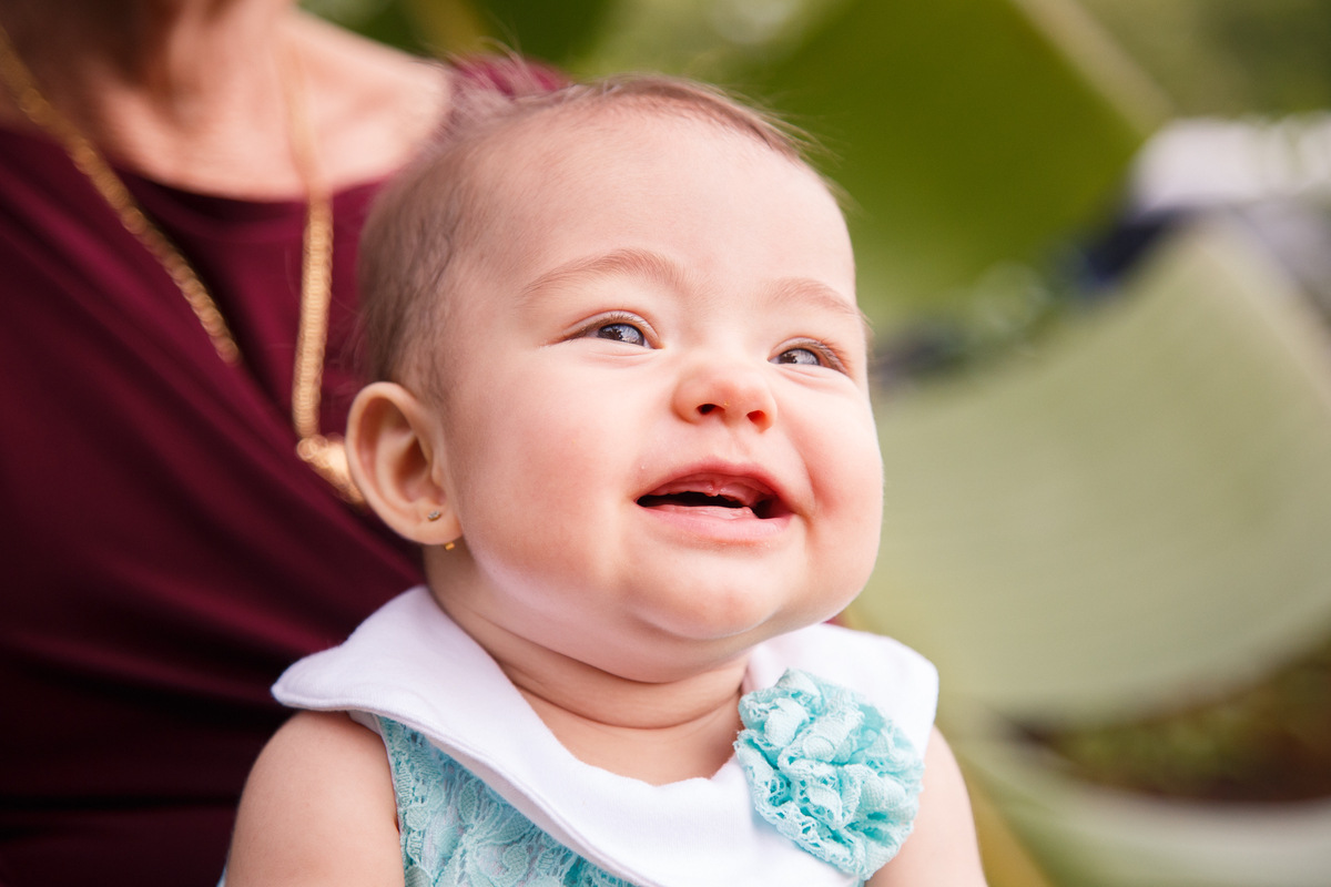 Bebê com a gengiva começando a ficar inchada para nascerem dentes, sentada no colo da bisavó e sorrindo.