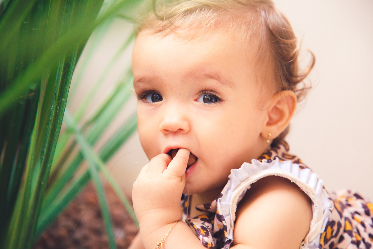 Bebê com dente coçando colocando um objeto na boca para coçar a gengiva.