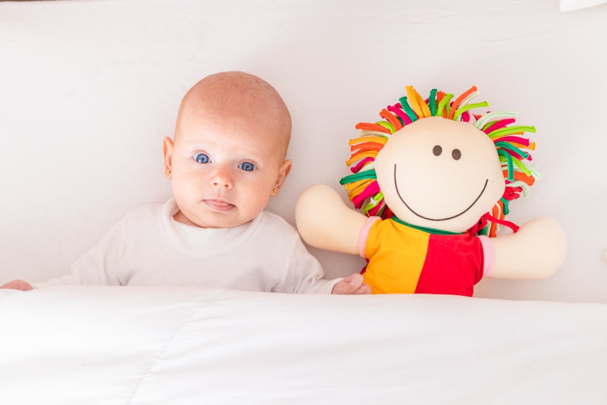 bebê recém nascido deitado com boneca olhando para a foto