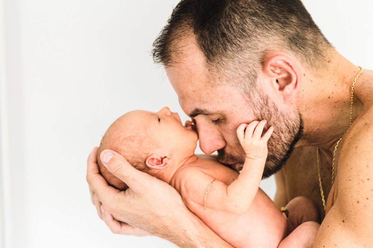 pai segurando bebê recém nascido nos braços e beijando a barriga do bebê