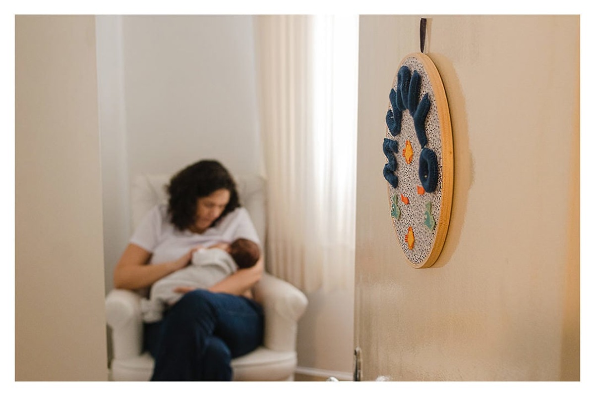 enfeite de quarto de bebê recém nascido mamando com mãe, durante a sessão de fotos de newborn lifestyle em Curitiba, do fotógrafo infantil e de família Rapha Luna