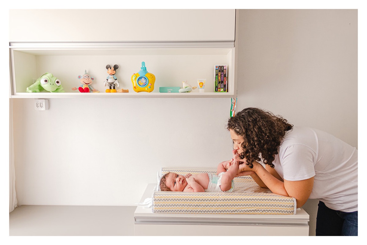 mãe brincando com os pés do bebê recém nascido deitado no trocador no quarto, durante a sessão de fotos de newborn lifestyle em Curitiba, do fotógrafo infantil e de família Rapha Luna