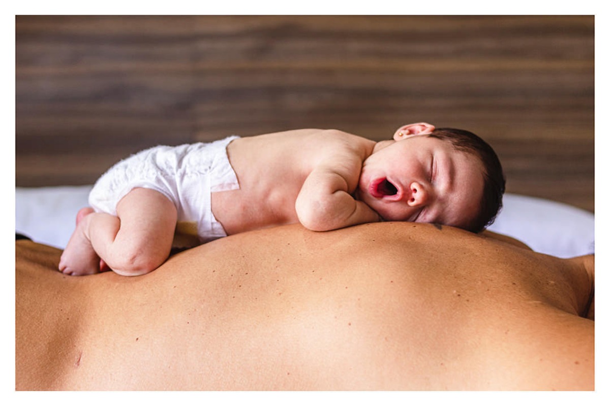 bebê recém nascida bocejando de boca aberta deitada nas costas do pai durante a sessão de fotos de newborn lifestyle em Curitiba, do fotógrafo infantil e de família Rapha Luna