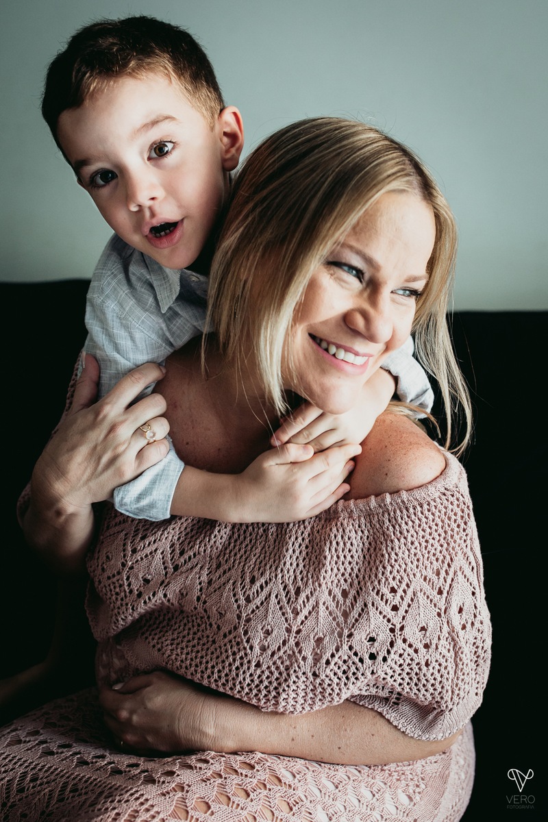 Filho abraça a mãe gestante no sofá da casa