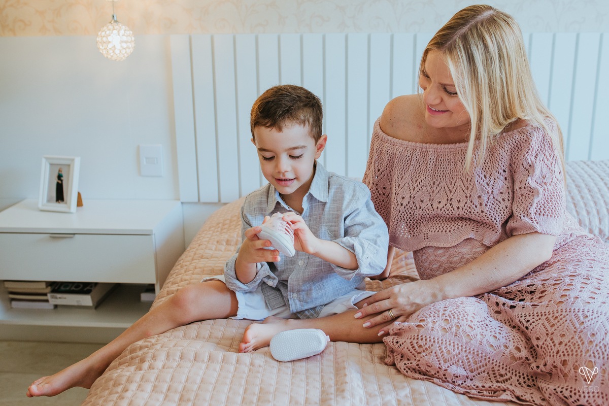 Mãe e filho brincam com sapato de bebê da irmã que vai nascer