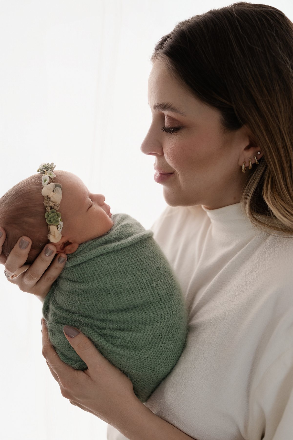 Mãe de blusa off-white olha para a bebê envolta em manta verde