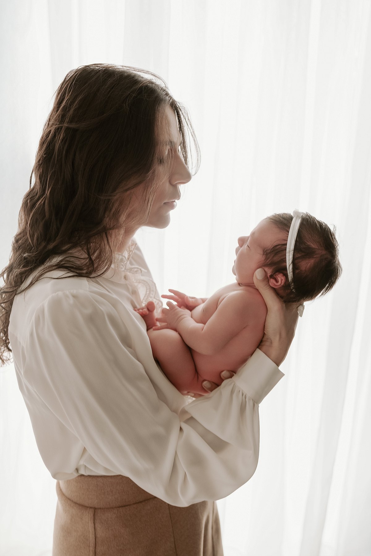 Mãe segurando o recém-nascido junto ao corpo, em luz de janela