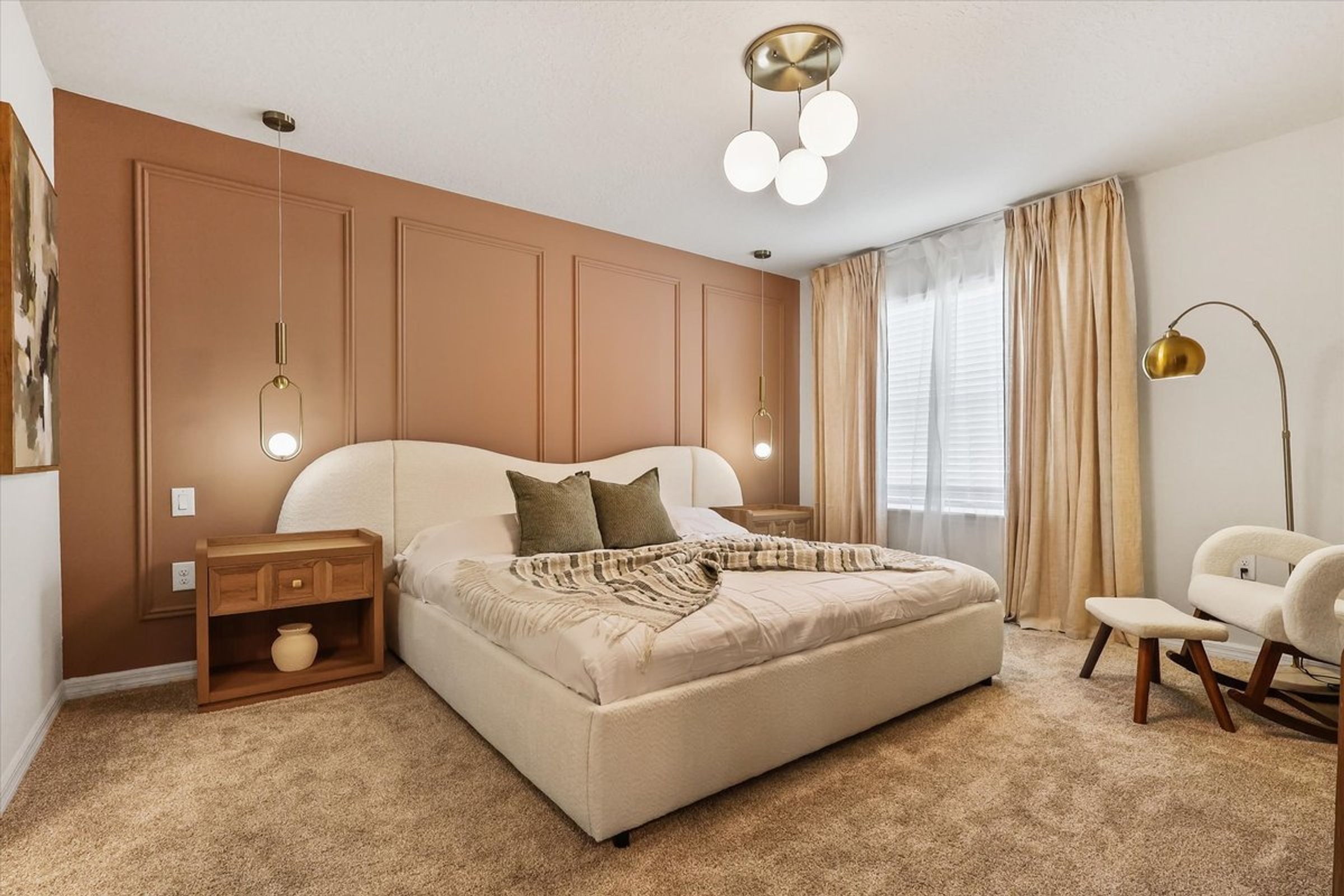 Bedroom with terracotta feature wall, upholstered bed, bedside lighting and a reading chair.