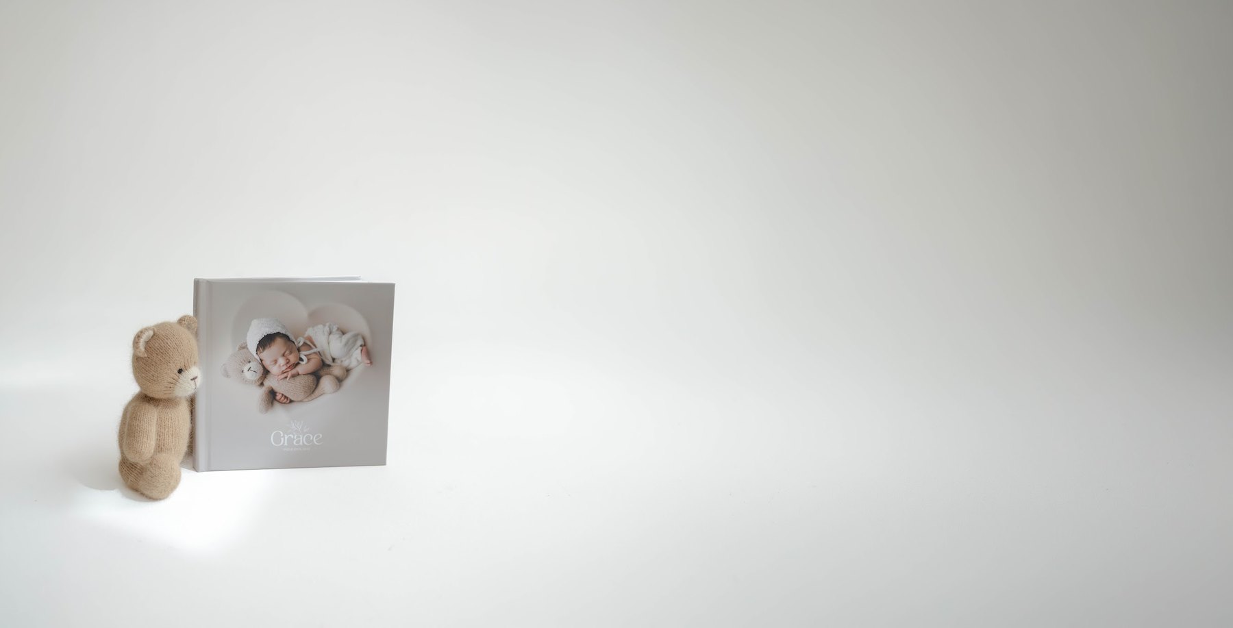Álbum fotográfico newborn com capa fotográfica, ao lado de um ursinho de pelúcia