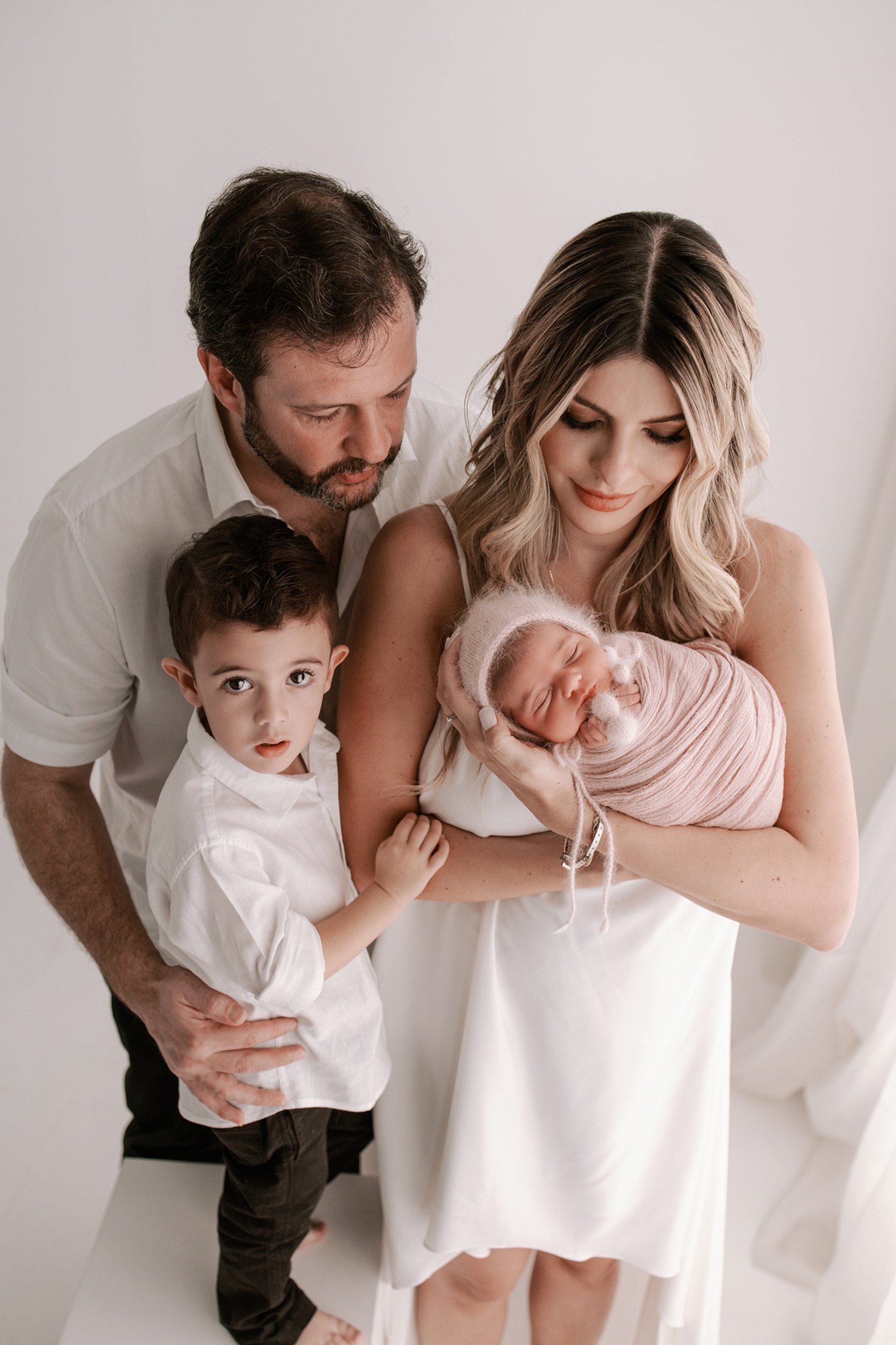 Pais e irmão com o bebê recém-nascido durante o ensaio newborn
