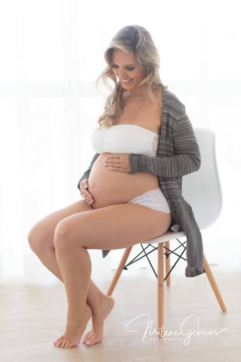 gestante sentada em cadeira branca fundo branco barriga aparente'