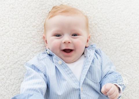 bebê ruivo 4 meses menino fundo claro deitado sorrindo camisa'