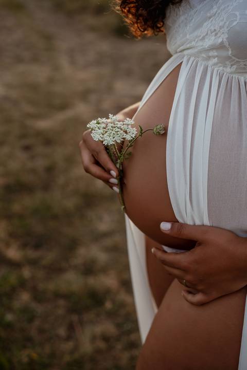 Casal grávido com filha pequena durante sessão fotográfica de família ao ar livre.'