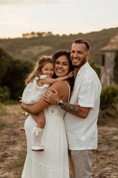Menina entrega flor à mãe grávida durante sessão fotográfica em família no exterior.'