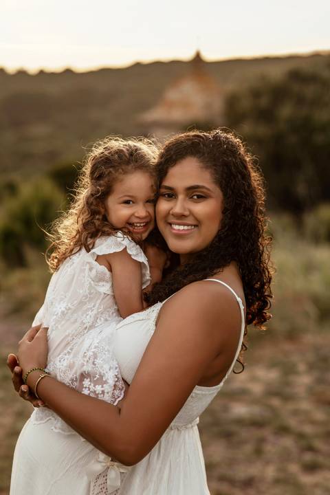 Mulher grávida abraçada à filha pequena durante sessão fotográfica de maternidade em Lisboa.'