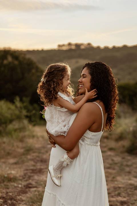 Mulher grávida abraçada à filha pequena durante sessão fotográfica de maternidade em Lisboa.'