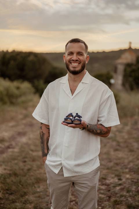 Futuro pai segura sapatinhos de bebé durante sessão fotográfica de maternidade.'