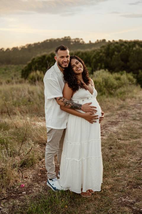 casal grávido com filha pequena durante sessão fotográfica de família ao ar livre.'
