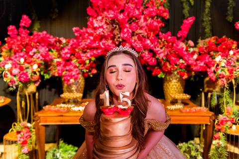 Debutante Júlia comemorando seus 15 anos diante da mesa do bolo e da decoração da festa.'