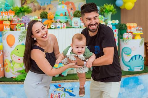 Pais sorrindo com Gustavo ao centro, registrando um momento especial da comemoração do seu primeiro aniversário.'