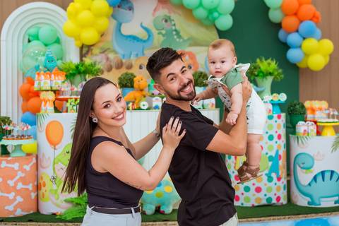 Pais sorrindo com Gustavo ao centro, registrando um momento especial da comemoração do seu primeiro aniversário.'