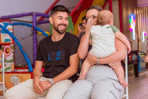 Gustavo no colo do pai, com a mãe ao lado, em um momento de alegria durante a comemoração do seu primeiro aninho.'