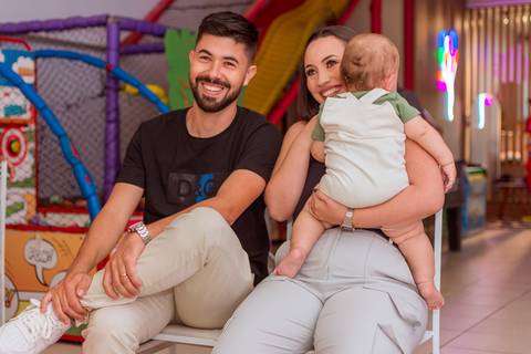 Gustavo no colo do pai, com a mãe ao lado, em um momento de alegria durante a comemoração do seu primeiro aninho.'