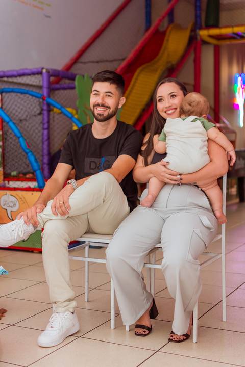 Gustavo no colo do pai, com a mãe ao lado, em um momento de alegria durante a comemoração do seu primeiro aninho.'