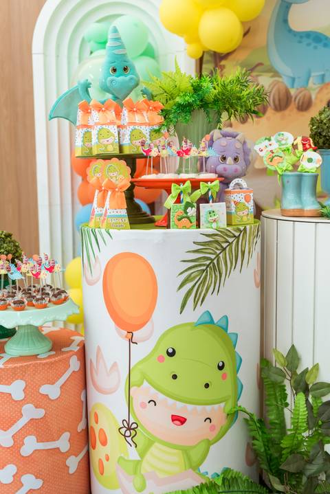 Detalhes da decoração infantil com dinossauros coloridos, doces personalizados e elementos tropicais na festa do Gustavo.'