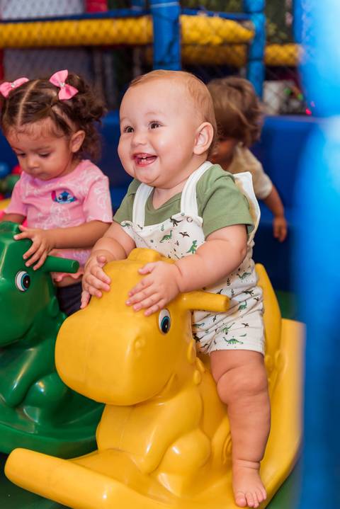 Gustavo sorrindo enquanto brinca em um brinquedo amarelo no espaço infantil da sua festa de aniversário.'