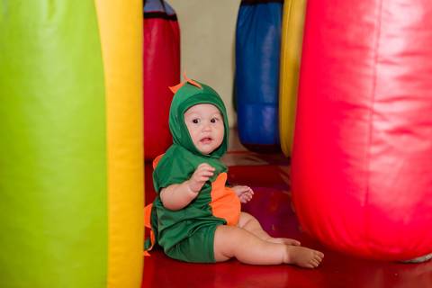 Gustavo sentado no brinquedo inflável colorido, explorando o espaço de diversão durante seu aniversário de 1 aninho.'