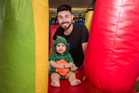 Pai sorrindo atrás de Gustavo enquanto os dois se divertem juntos no brinquedo inflável durante a festa infantil em Tatuí.'