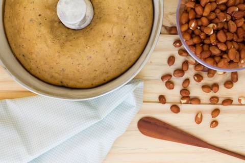bolo de amendoim sobre uma mesa de madeira clara com alguns amendoins caídos sobre a mesa'