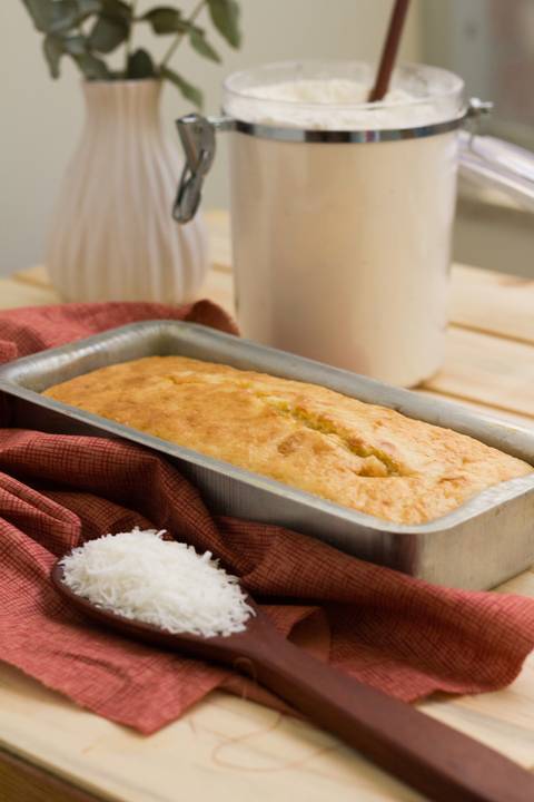 bolo de como sobre uma mesa onde também vemos lascas de coco fresco farinha de trigo e leite'
