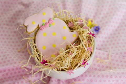 biscoito decorado em forma de coelhinho da pascoa dentro de um pequeno ninho feito com palha e flores'