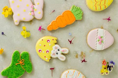 biscoitos de páscoa decorados sobre a superfície de mármore branco com algumas flores naturais'