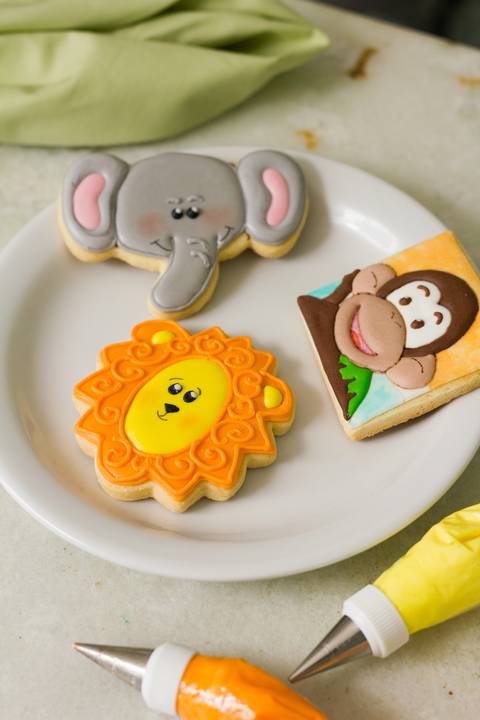 biscoitos decorados com a temática animal, feitos para a empresa macakids. Biscoitos em formato de elefante, leão e macaco sobre um prato branco'