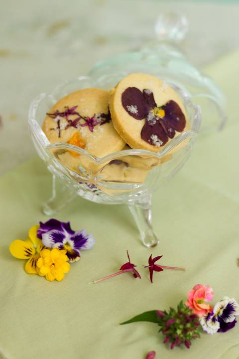 biscoitos amanteigados com flores comestíveis delicadamente colocados dentro de um pote de louça'