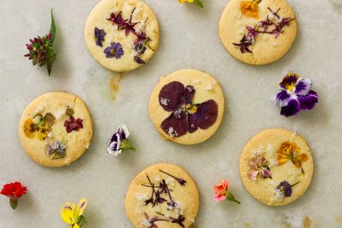 biscoitos amanteigados floridos sobre a superfície de mármore branco enfeitado com flores comestíveis'