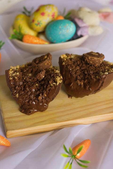 ovo de páscoa artesanal de colher feito em chocolate nobre partido ao meio sobre uma pequena tábua de madeira onde vemos o recheio do interior escorrendo sobre a tábua'