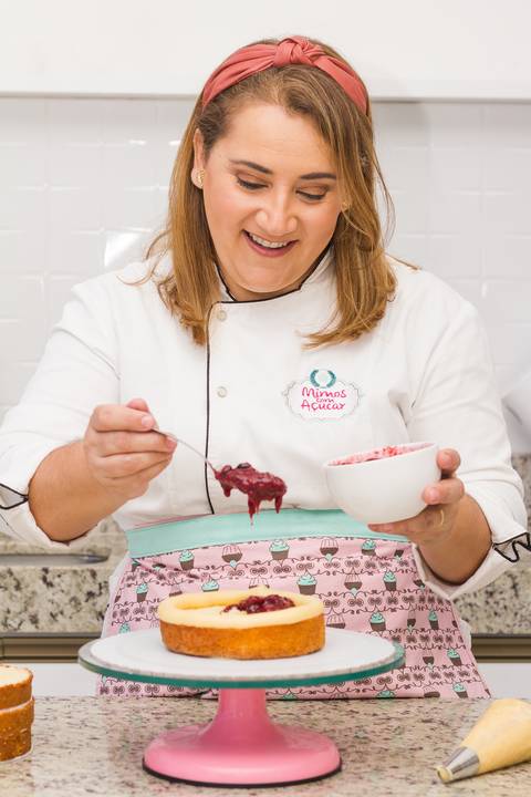 Chef confeiteira segurando um pote com geleia de frutas vermelhas em uma cozinha bem iluminada durante o dia'