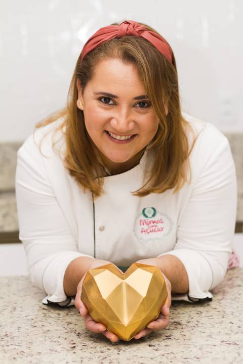 chef confeiteira jovem posa para foto de maneira descontraída apoiada sobre uma bancada de mármore'