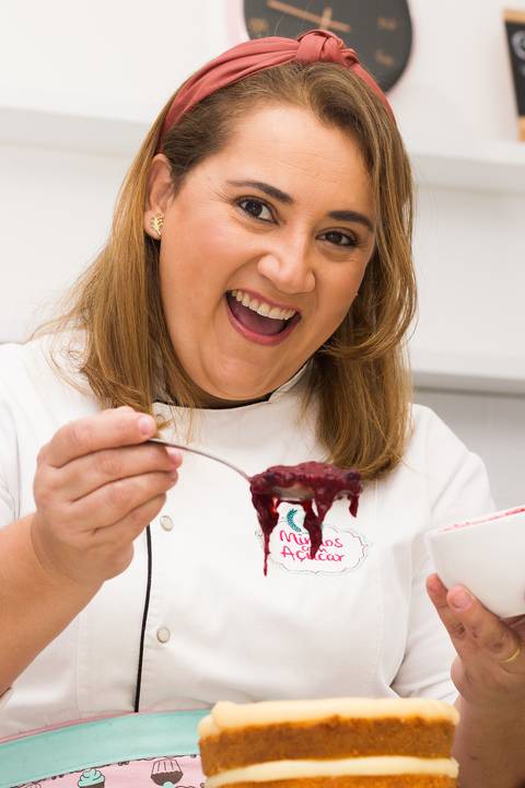  chef ludmila da mimos com açúcar segurando uma colher farta de geleia de frutas vermelhas em que recheia um pequeno naked cake de massa branca'
