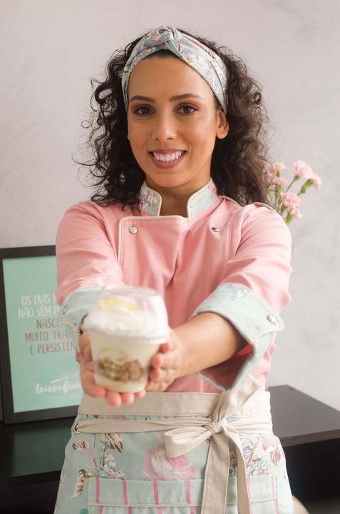 Chef confeiteira vestindo dolmã rosa segurando copo da felicidade'