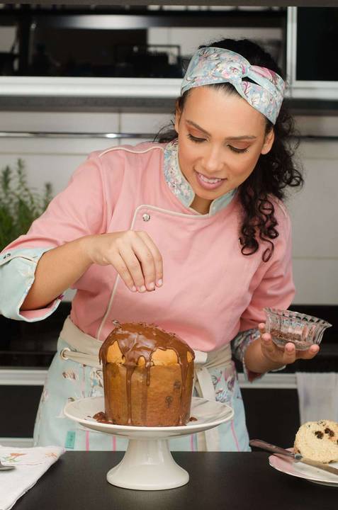 Mulher jovem e feliz decora com gotas de chocolate panetone recém coberto com uma deliciosa calda de chocolate '