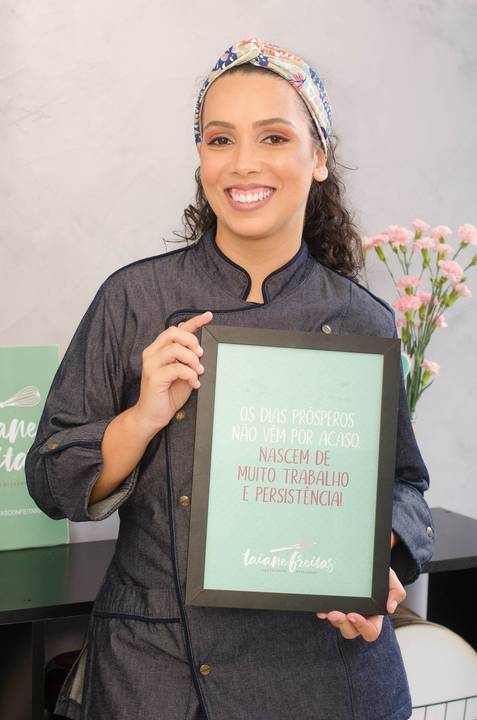 Taiane Freitas confeitaria posa segurando um quadro com mensagem motivacional em seu ateliê localizado em Vila Velha'